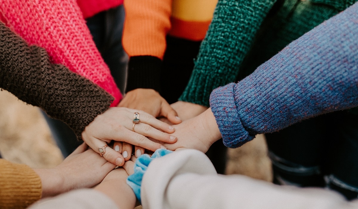 Eight individuals join their hands together in the centre of a circle