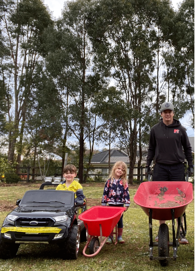 Ben is gardenning with his two children each boasting a wheelbarrow or mini car