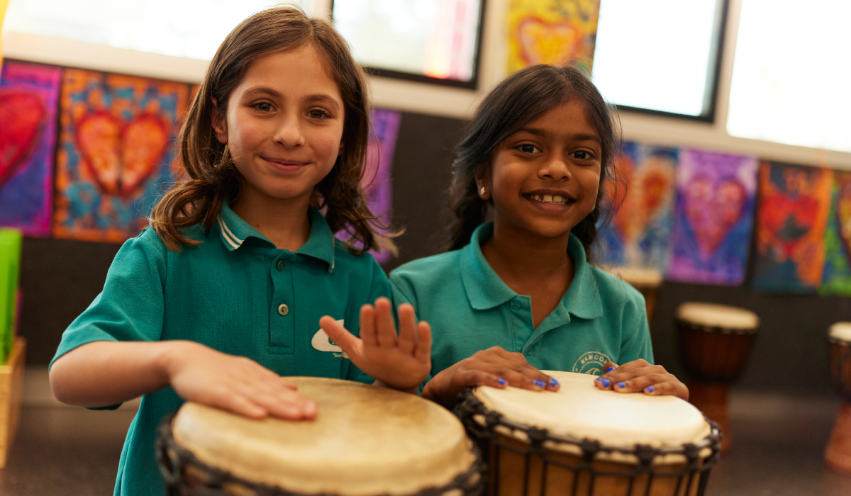 Two young female primary school students play a hand drum