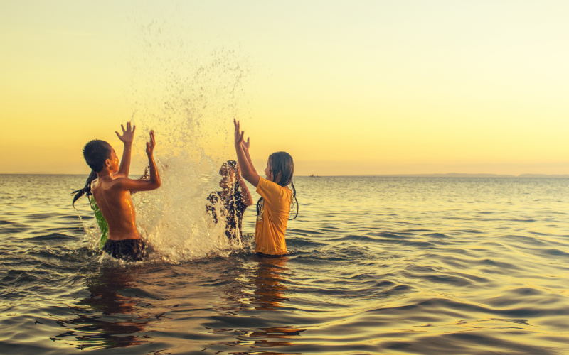 A group of children playing in the ocean against a sunset